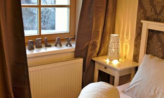 A cozy room with a window, curtains, and a nightstand. On the windowsill, the word "RELAX" is displayed along with a lit lamp.