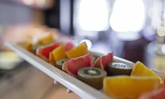 A colorful selection of fresh fruits on a white plate. The fruits consist of melon, kiwi, and orange.