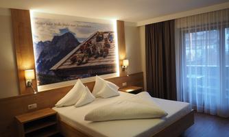 A modern bedroom with a double bed and stylish wooden furniture. On the wall, there is an artistic mural depicting an alpine landscape.
