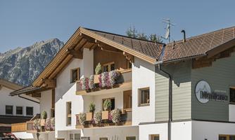 A charming building with traditional balconies, adorned with colorful flowers. In the background, majestic mountains can be seen.