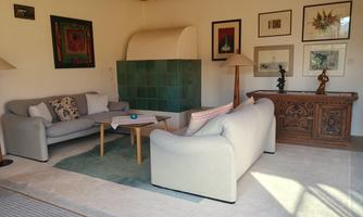 A cozy living room with two sofas and a small coffee table. The walls are decorated with artwork, and a fireplace provides a warm atmosphere.