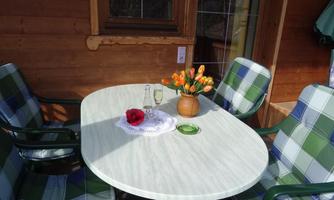 A cozy table with chairs in a wooden house. On the table there is a vase with tulips and a glass.