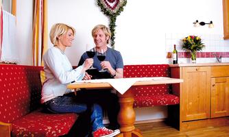 A cozy interior with a table and red seating. A couple toasts each other with wine glasses and enjoys their time together.