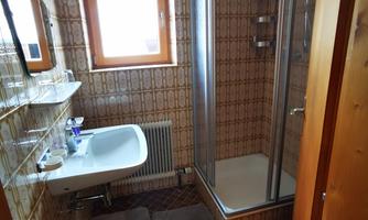 A small bathroom with a shower, a sink, and a window. The walls are decorated with traditional tiles.