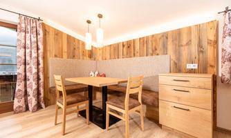 A cozy dining area with a wooden table and chairs. The walls are clad with wooden panels and the windows are adorned with decorative curtains.