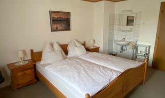 A simple bedroom with a double bed and two nightstands. A picture hangs on the wall, and there is a sink in the room.