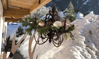 A beautiful winter view with snow-covered mountains. A rustic chandelier with pine branches and decorations hangs from a wooden veranda.
