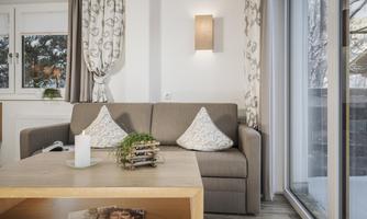 A cozy living room with a gray sofa and decorative cushions. A wooden coffee table and large windows bring in plenty of daylight.