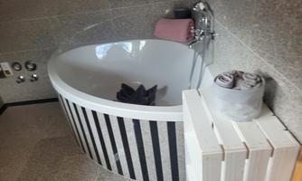 A modern bathtub with an elegant striped design is situated in a room with gray walls. Next to the bathtub are clean towels and a convenient towel holder.