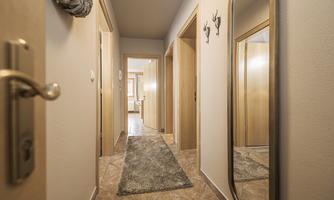 A bright hallway with a carpet and several doors. A mirror hangs on the wall, making the room appear larger.