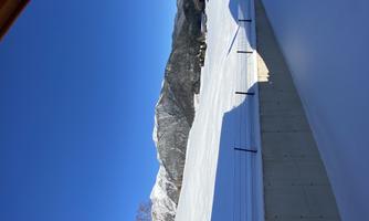 A winter landscape with snow-covered fields and tall mountains in the background. The clear blue sky makes the scene bright and inviting.