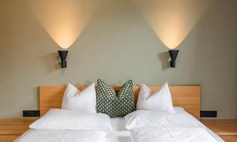 A modern bedroom with a large bed and stylish pillows. The walls are painted in soft colors and illuminated with wall lights.