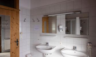 A modern bathroom with two sinks and a large mirror. The walls are tiled, and there are wooden accents on the door.