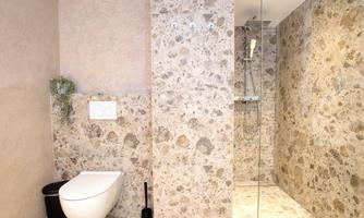 A modern bathroom with elegant stone walls and a shower. The toilet is stylishly and functionally integrated into the space.