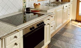 A modern kitchen with light cabinets and an elegant workspace. The floor is laid with square tiles, and light streams through the window.