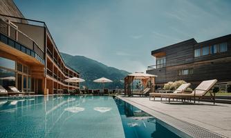 A modern hotel with a stylish pool and sun loungers. The mountains provide an impressive backdrop in the background.