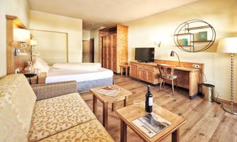 A cozy hotel room with a large bed, a sitting area, and a desk. The room is bright and furnished in a modern style.