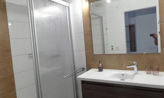 A modern bathroom with a shower and a sink. The mirror reflects soft light and the walls are brightly tiled.