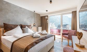 A modern bedroom with a large bed and stylish decoration. The room has large windows that offer a view of the mountains.