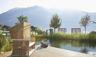 A quiet place by the water with cozy loungers and a view of the mountains. Green plants and a peaceful atmosphere invite you to relax.