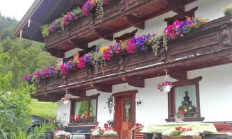 A traditional wooden house with colorful flower balconies. The surroundings are green and inviting.