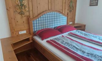 A cozy bedroom with a wooden bed and red pillows. The walls are decorated with a rustic wood pattern.