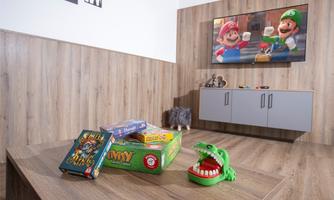 A cozy playroom with a wooden floor and a television wall. Various board games and a toy crocodile are on the table.