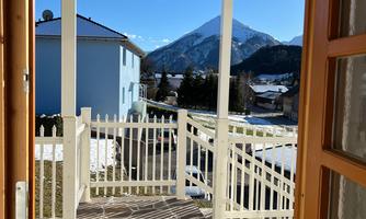 A view through the door onto a terrace with a beautiful outlook over the mountains. The sun shines brightly in the blue sky.