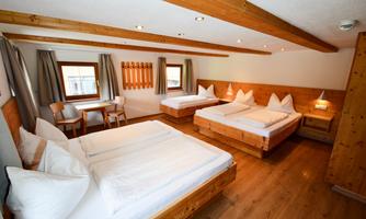 A spacious room with two double beds and one single bed. The wooden ceilings and light curtains give the room a cozy atmosphere.