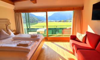 A cozy hotel room with two beds and a red couch. Large windows offer a beautiful view of the mountains and the landscape.