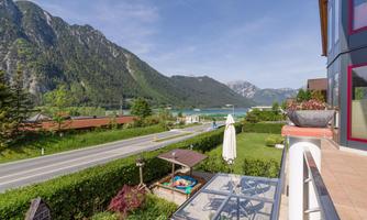 A beautiful mountain landscape with lush greenery and a clear blue sky. In the foreground, there is a road and a well-maintained garden.