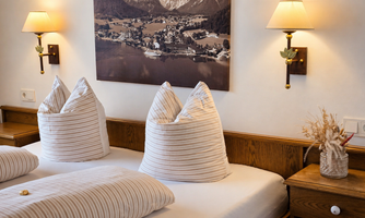 A cozy bedroom with a double bed and decorative pillows. On the wall, lamps and a landscape picture are hanging.