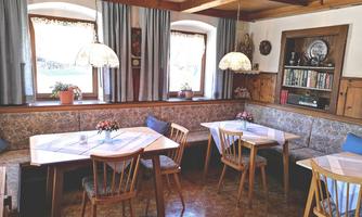 A cozy dining room with paneled wooden walls and a rustic atmosphere. Large windows let in plenty of light, and the tables are simply set.