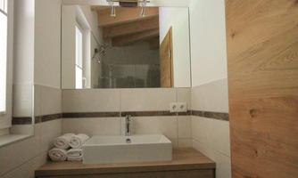 A modern bathroom with a wooden sink and a large mirror. The walls are brightly tiled and the light is warm and inviting.