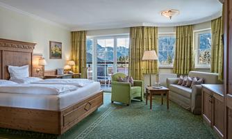 A bright room with a large bed and cozy seating. Large windows provide a view of the mountains and let in plenty of daylight.