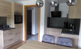 A modern kitchen with wooden cabinets and a dining area. The lighting is complemented by elegant hanging lamps.
