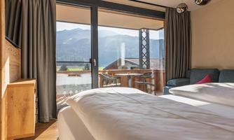 A modern bedroom with a view of the mountains. Large windows let in a lot of light and lead to a balcony.