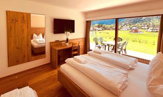 A modern bedroom with a large window and a view of the landscape. The decor is made of wood and offers a cozy atmosphere.
