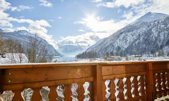 A beautiful view of snow-capped mountains and a lake. The sun shines in the blue sky, creating a picturesque atmosphere.