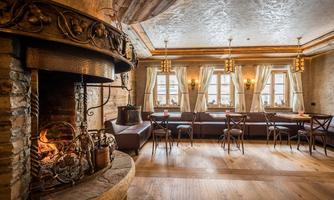 A cozy room with a rustic fireplace and wooden furniture. Large windows allow plenty of daylight and create an inviting atmosphere.