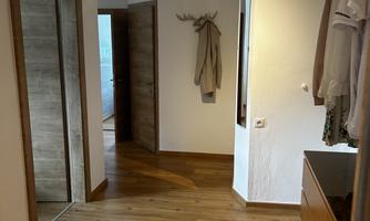 A bright hallway with wooden flooring and a coat rack. The room has a friendly atmosphere and access to other rooms.