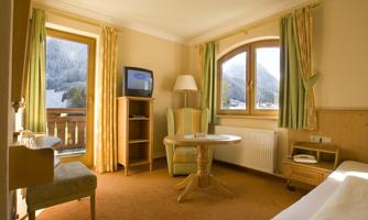 A cozy hotel room with a table, two chairs, and a small television. The windows offer a beautiful view of the mountains.