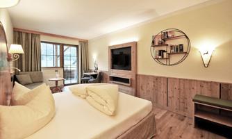 A cozy hotel room with wooden furniture and a large window. The amenities include a television, an armchair, and a small seating area.