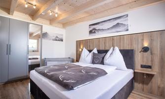 A modern bedroom with a comfortable bed and wooden details. Large windows let in plenty of light and create a cozy atmosphere.