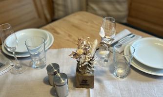A beautifully set table with plates, glasses, and a small floral arrangement. The cozy bench in the background creates an inviting atmosphere.