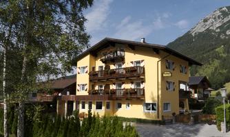 A cozy yellow building with balconies and beautiful windows. In the background, mountains and green grass are visible.