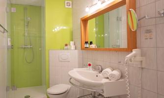 A modernly furnished bathroom with a shower and a bright green wall. Fresh towels are placed on the sink and toiletries are neatly arranged.