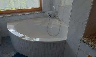 A modern bathroom with an oval bathtub and a window that lets in light. The floor is equipped with gray tiles and a blue rug.