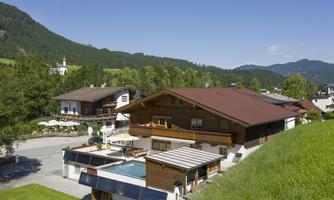 A picturesque alpine house with a pool in the foreground. Surrounded by green hills and a clear blue sky landscape.