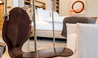 A cozy interior with a wooden swing and a modern bed in the background. The atmosphere is warm and inviting.